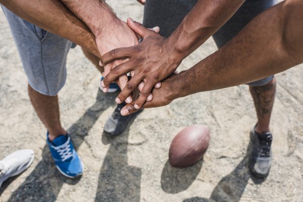Hand-stack gesture in a huddle with a football on the ground